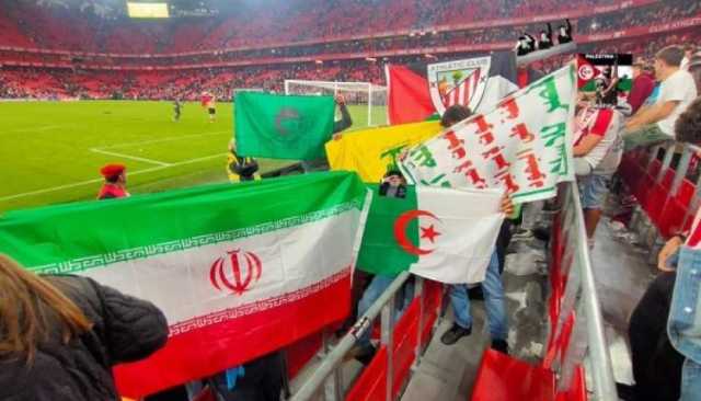 مشجعون في اسبانيا لكرة القدم يرفعون شعار الصرخة وأعلام دول محور المقاومة